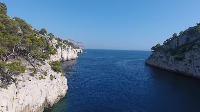 Drone view flying over the mediterranean sea, getting out of a creek. Sunny day, cliffs and trees. Cassis in background