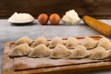 Fototapeta na wymiar Dumplings with filling, laid out on the kitchen cutting Board on the background of ingredients-flour, cottage cheese, chicken eggs.