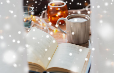 christmas, hygge and winter concept - book and cup of coffee or hot chocolate on table over snow