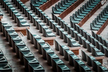Free unclaimed seats in multiple rows. Sunset photo in empty public arena and concert amphitheatre. Red brick and white travertine structure, gray plastic chairs. 