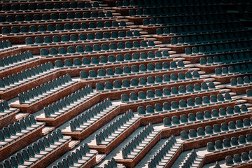Obraz premium Free unclaimed seats in multiple rows. Sunset photo in empty public arena and concert amphitheatre. Red brick and white travertine structure, gray plastic chairs. 