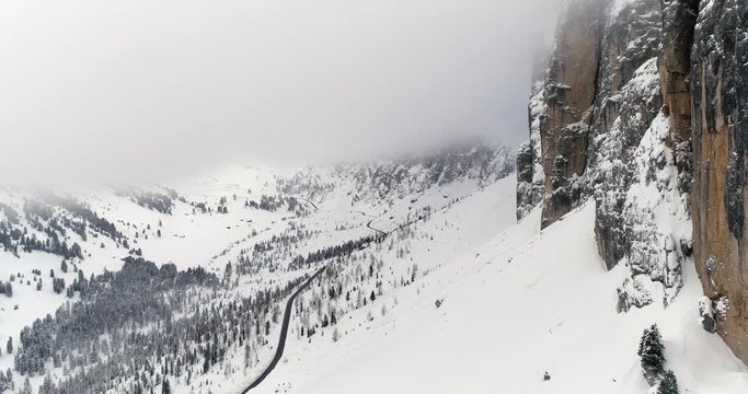 Forward aerial with snowy mountain,road and woods forest at Sella pass.Cloudy bad overcast foggy weather.Winter Dolomites Italian Alps mountains outdoor nature establisher.4k drone flight