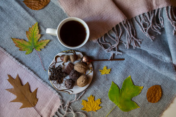A cup of tea and sweet snacks with decoration by autumn leaves on the warm plaid. Seasonal still life.