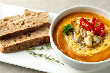 Cup with tasty pumpkin cream soup on plate, closeup