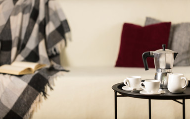Fototapeta na wymiar Round black metal coffee table with a coffee maker and a cup on the background of a white sofa with a gray blanket.