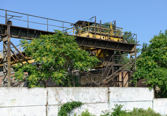 Rusted constructions of overhead crane are behind concrete fence.