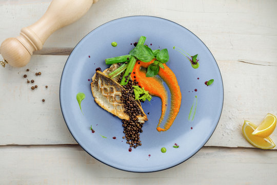 Plate with delicious grilled seabass fish fillet steak and vegetables on a white wooden table. Healthy gourmet food.Directly above top view shot.