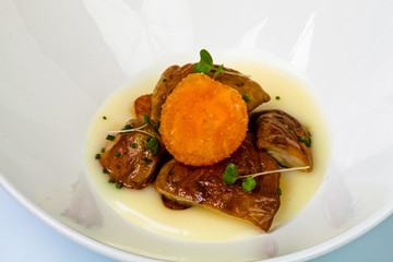 Setas salteadas sobre patata chafada y ravioli de huevo frito