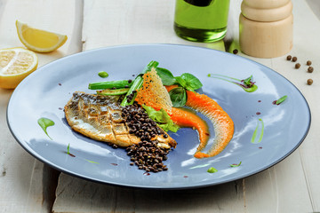 Grilled seabass fish fillet steak with vegetables on a plate. Healthy gourmet seafood meal on a table. Close-up shot.