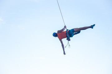 View of man in hardhat hanging on rope while doing rappel and showing pirouettes flying in air  © pablobenii