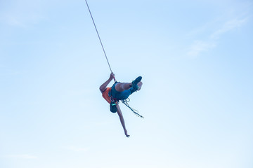 View of man in hardhat hanging on rope while doing rappel and showing pirouettes flying in air  © pablobenii