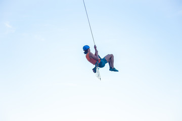 Fototapeta na wymiar View of man in hardhat hanging on rope while doing rappel and showing pirouettes flying in air 