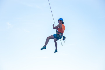 View of man in hardhat hanging on rope while doing rappel and showing pirouettes flying in air 