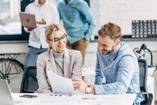 smiling young business colleagues working with papers in office