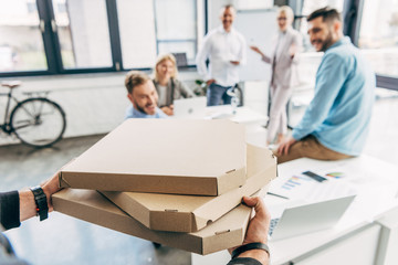 cropped shot of man bringing pizza to happy colleagues in office