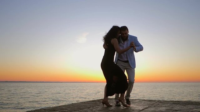 Portrait of young attractive couple dancing latin bachata near sea or ocean. Sunlight background. Summer time, romantic footage. Slow motion