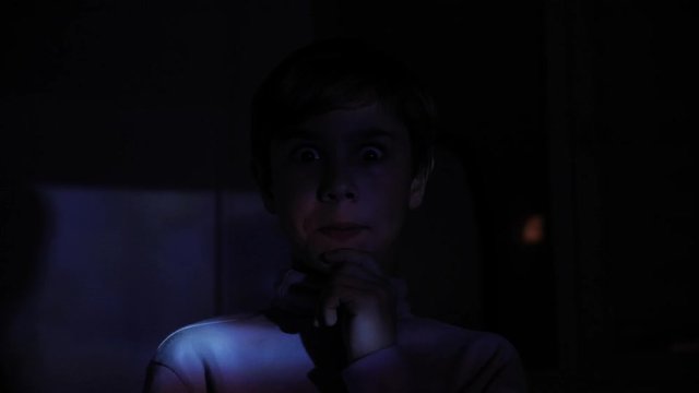 Little Scared Boy watching Horror Film or Video on TV or Computer in the Dark room. Reflection on his face.