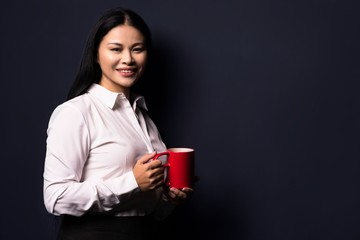 Businesswoman enjoying coffee break holding red cup. Standing half turn and smiling.