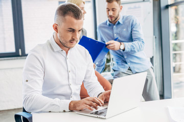 young businessman using laptop and colleagues working behind in office