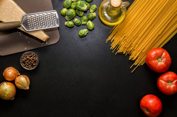 Flat lay, top view, space for text. Ingredients for italian pasta. Spaghetti, tomatoes, oil, onion, parmezan on black wooden background.