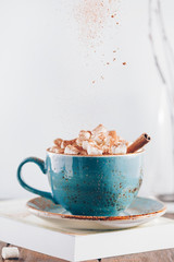 Hot chocolate with marshmallows and cinnamon stick in a blue ceramic cup on a table with a book. The concept of winter or fall time. Minimal scandinavian design.