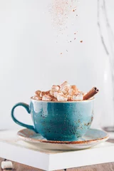Poster Hot chocolate with marshmallows and cinnamon stick in a blue ceramic cup on a table with a book. The concept of winter or fall time. Minimal scandinavian design. © Edalin