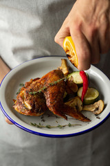 man holds a plate with baked chicken, lemon and vegetables.