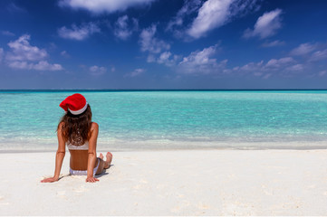 Fototapeta na wymiar Attraktive Frau im Bikni und Weihnachtsmütze genießt ihren Winterurlaub am tropischen Strand