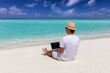 Geschäftsmann im Urlaub sitzt am tropischen Strand mit seinem Laptop und arbeitet