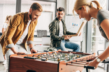 group of happy young casual business people playing table football at office and having fun together