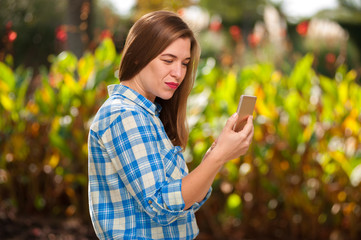 Beautiful young woman taking selfie on a smartphone against the backdrop of a green sunny park on a warm summer day