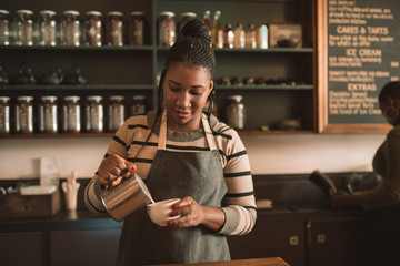 Smiling young African barista pouring milk into a cappuccino