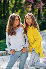Fototapeta premium Close-up portrait of friendly happy girls with posing in bright glasses outside. Two young ladies with lovely face expression spending time together and smiling to camera.