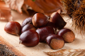 Chestnuts on wooden board and autumn leaves