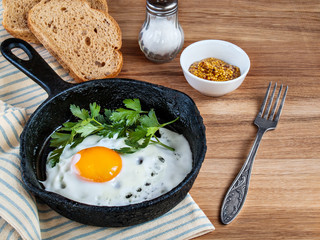 Fried eggs in a pan, bread, salt, fork on wooden background