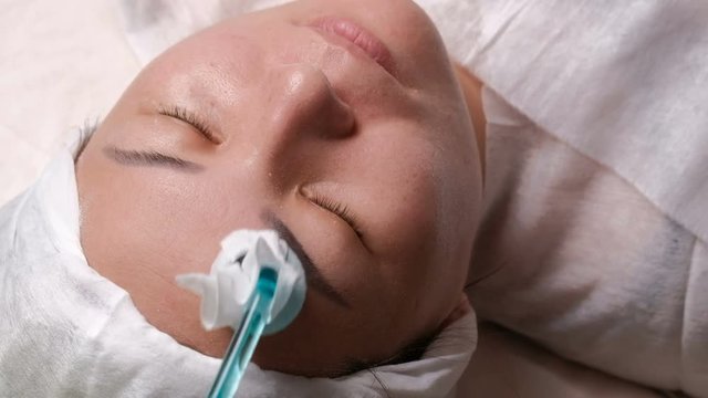 Darsonvalization. Close-up of the face of a Muslim woman on the physiotherapy facial rejuvenation procedure.The hands of a cosmetologist use a device with pulsed alternating currents of high frequency