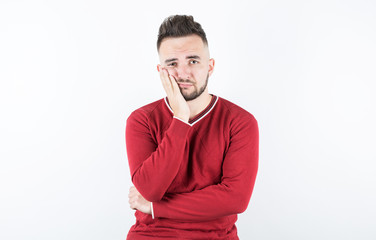 Portrait of a bored man with beard holding hand on cheek while support it with another crossed hand, over gray background.