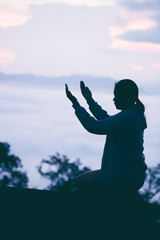 Silhouette of teen girl kneeling and praying over beautiful sunrise background.