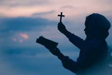 Silhouette of teen girl hands holding wooden cross and bible on sunrise background, Crucifix, Symbol of Faith.