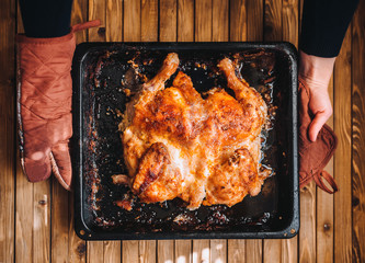 A pan with roast turkey in female hands. Thanksgiving Day. Homemade roasted chicken in a black pan on a wooden background. Lifestyle. Top view.