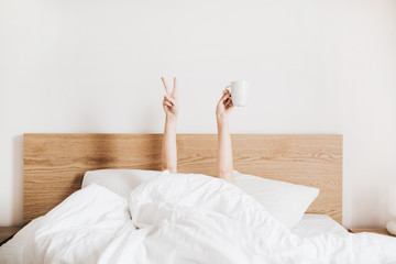 Hand's of young woman with coffee mug in bed with white linens. Minimal happy morning concept. - obrazy, fototapety, plakaty