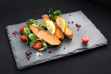 Rollo Gebackene Lachsstücke auf Salat. Abendessenteller auf einem schwarzen Teller. © Robert Przybysz