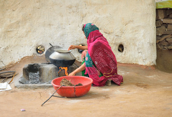 A woman cooking food in a stove made of mud.