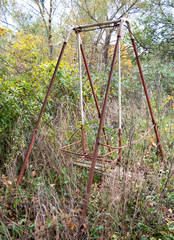 Fototapeta premium Old abandoned rusty swing among grass and trees