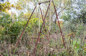 Old abandoned rusty swing among grass and trees