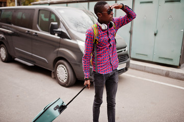 African american man in checkered shirt, sunglasses and earphones with suitcase and backpack. Black man traveler against van car. © AS Photo Family