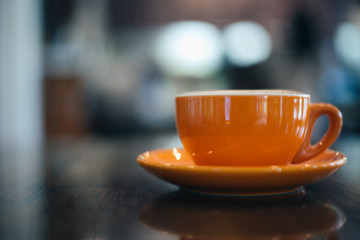 A orange cup of coffee on wooden background in coffee shop