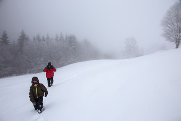 Hikers go up on snow slope in winter. Tourists trekking in winter mountains in fog