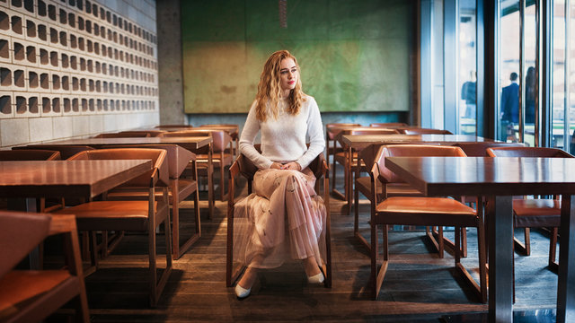 Good looking curly woman sitting in empty cafe . Indoor portrait of excited girl chilling on cozy chair. Panoramic photo