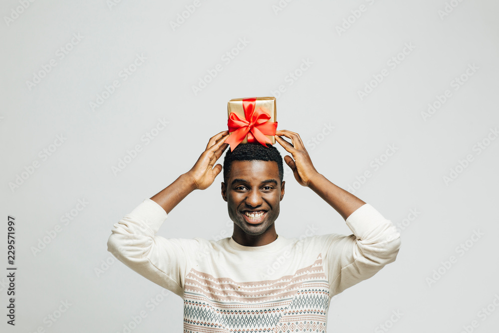 Wall mural Portrait of a smiling young man holding gift on his head, isolated on white studio background